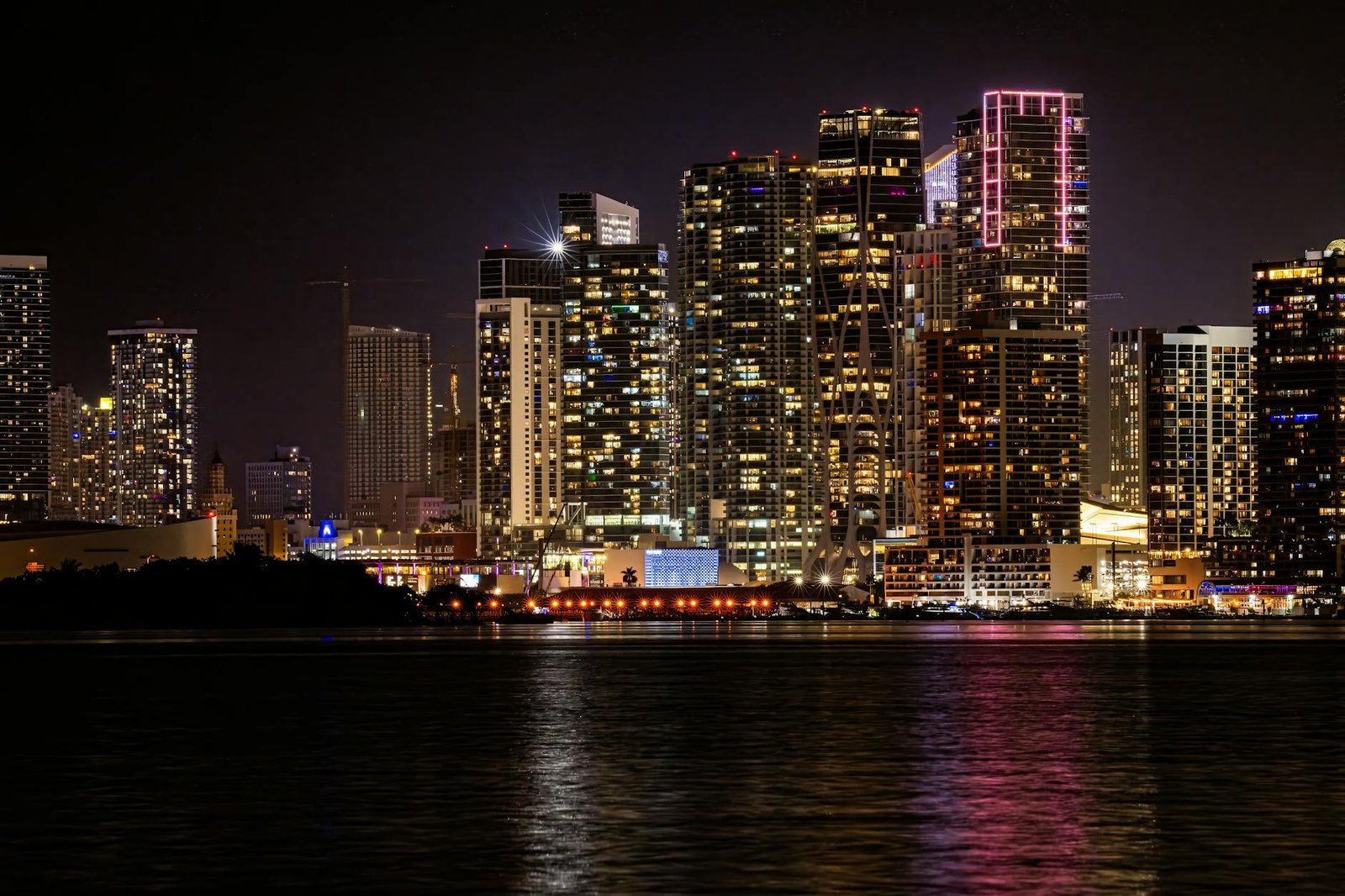 Vibrant Miami skyline illuminated at night, reflecting in the tranquil water.
