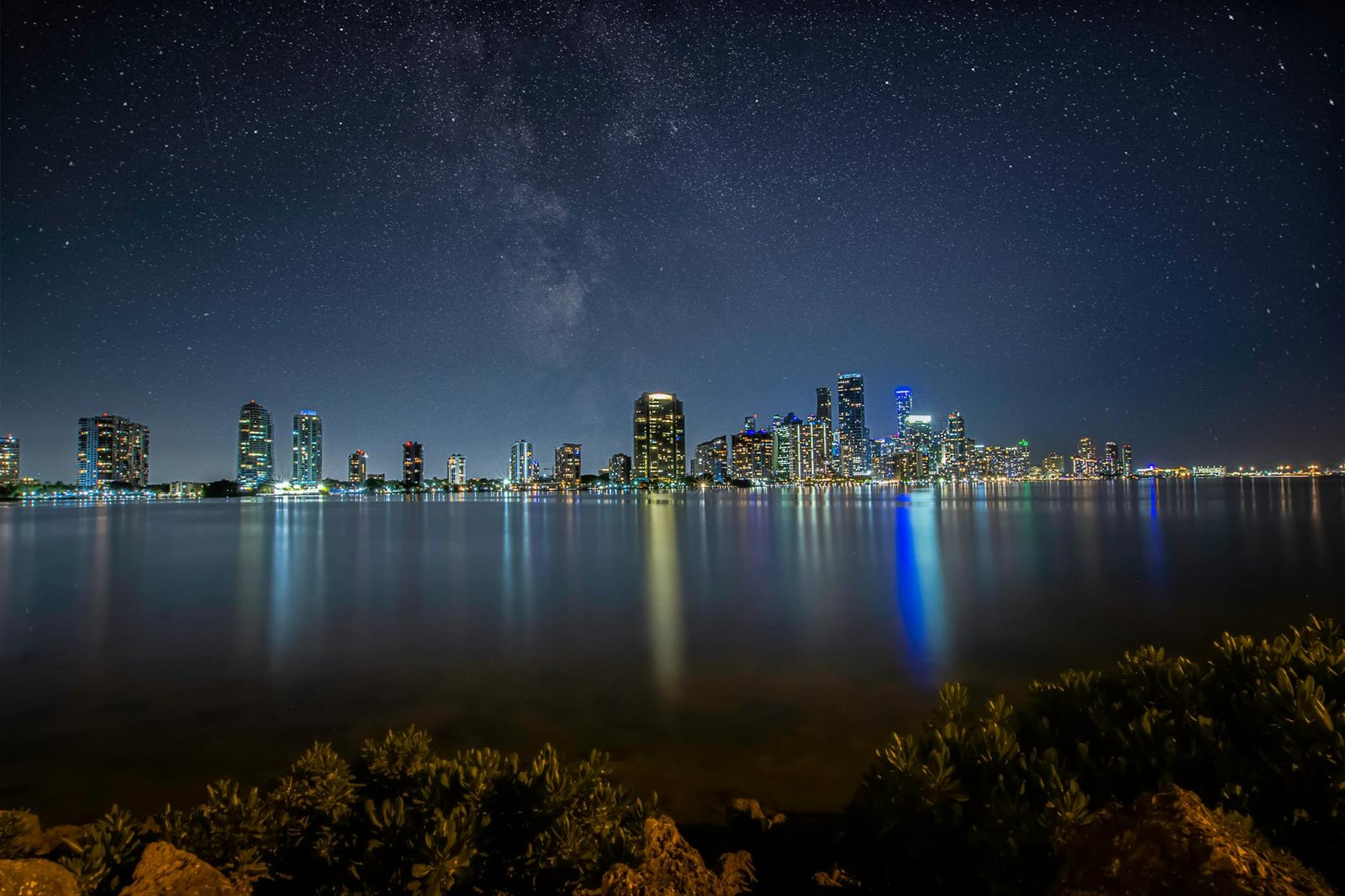 Breathtaking view of Miami's skyline at night with a star-filled sky reflecting over the water.