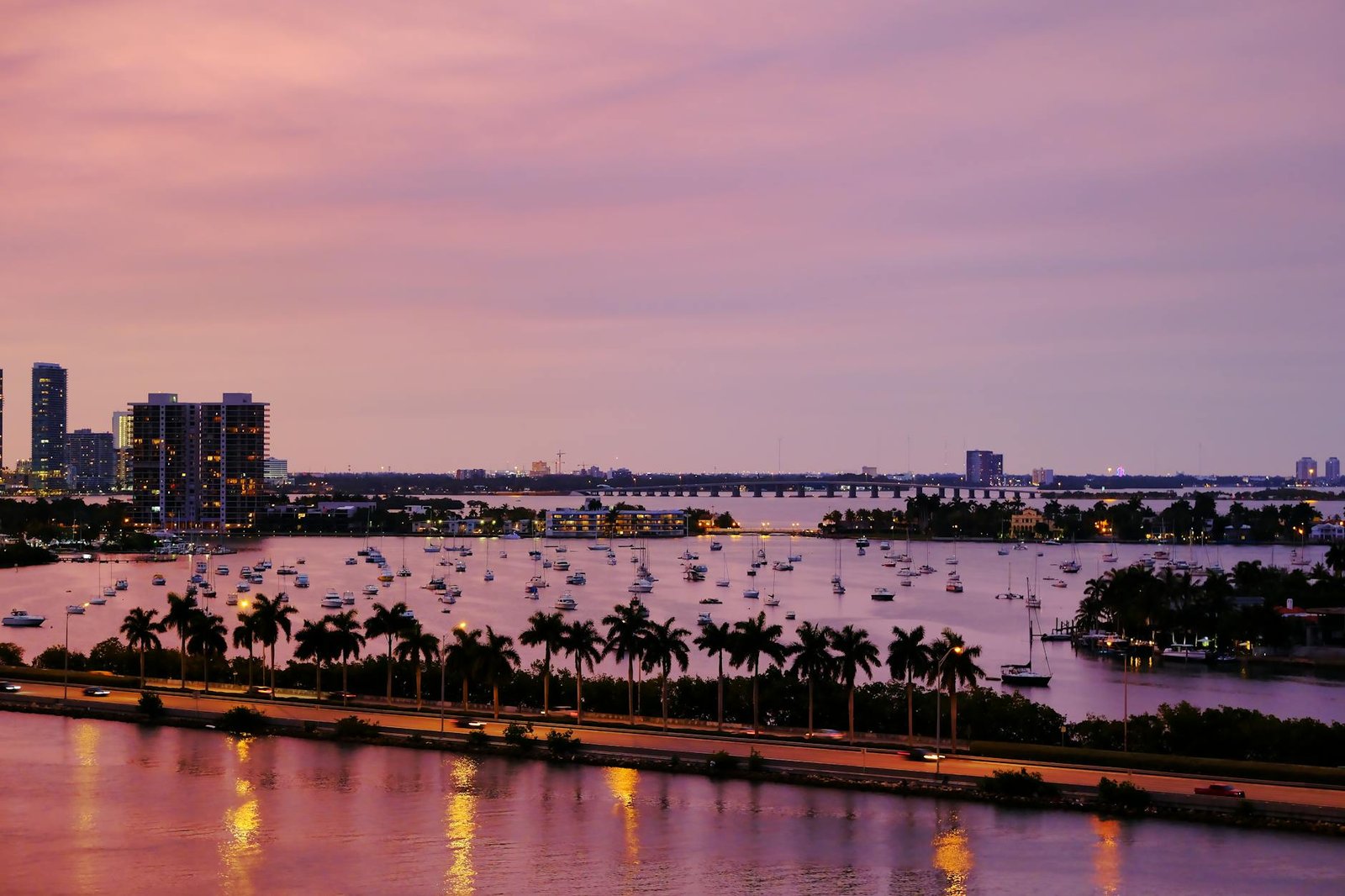 An aerial view of Miami's skyline at twilight, featuring water reflections and palm trees.