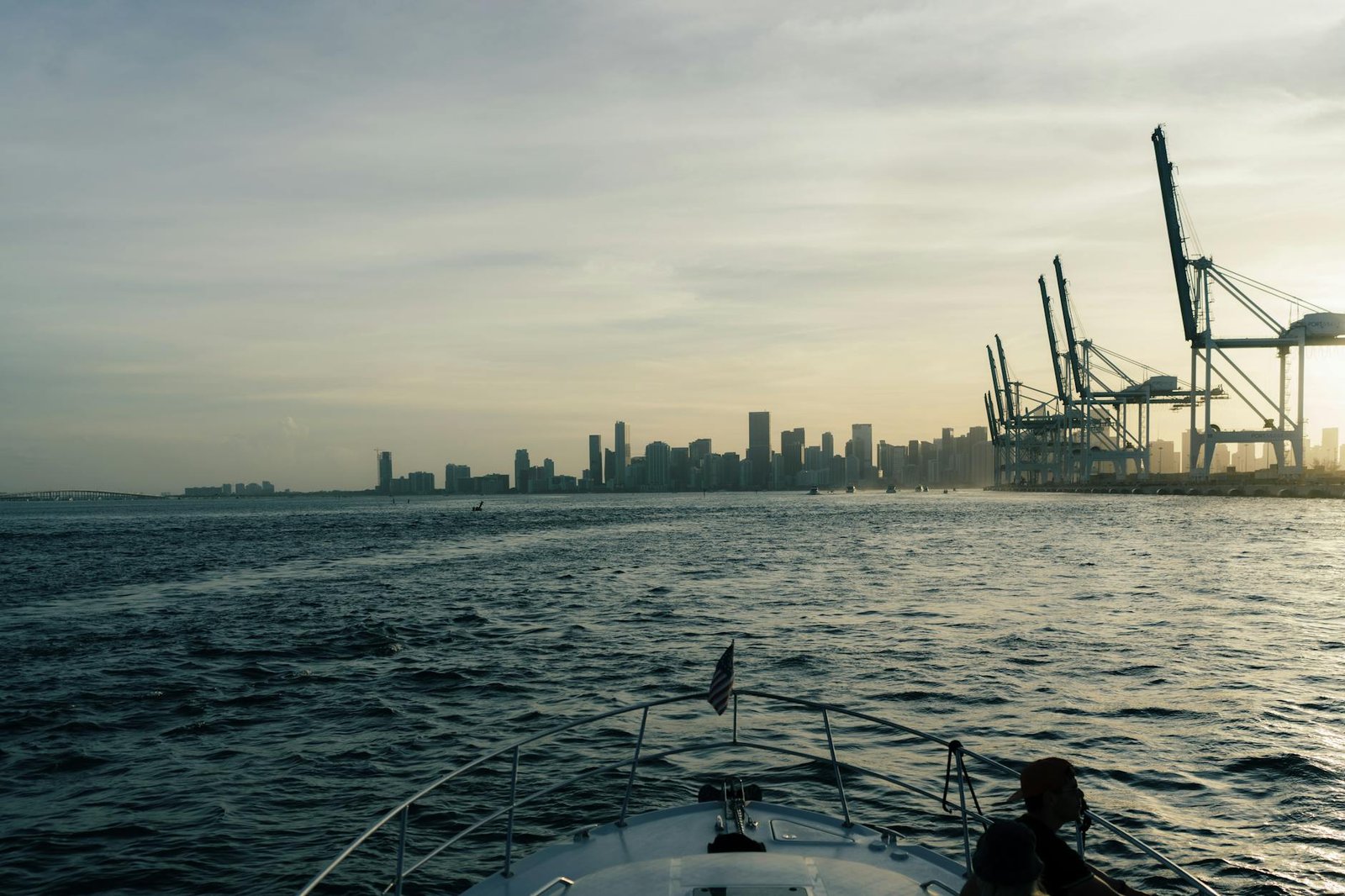Capture of Miami's skyline and harbor cranes during a tranquil sunset from a boat's deck.