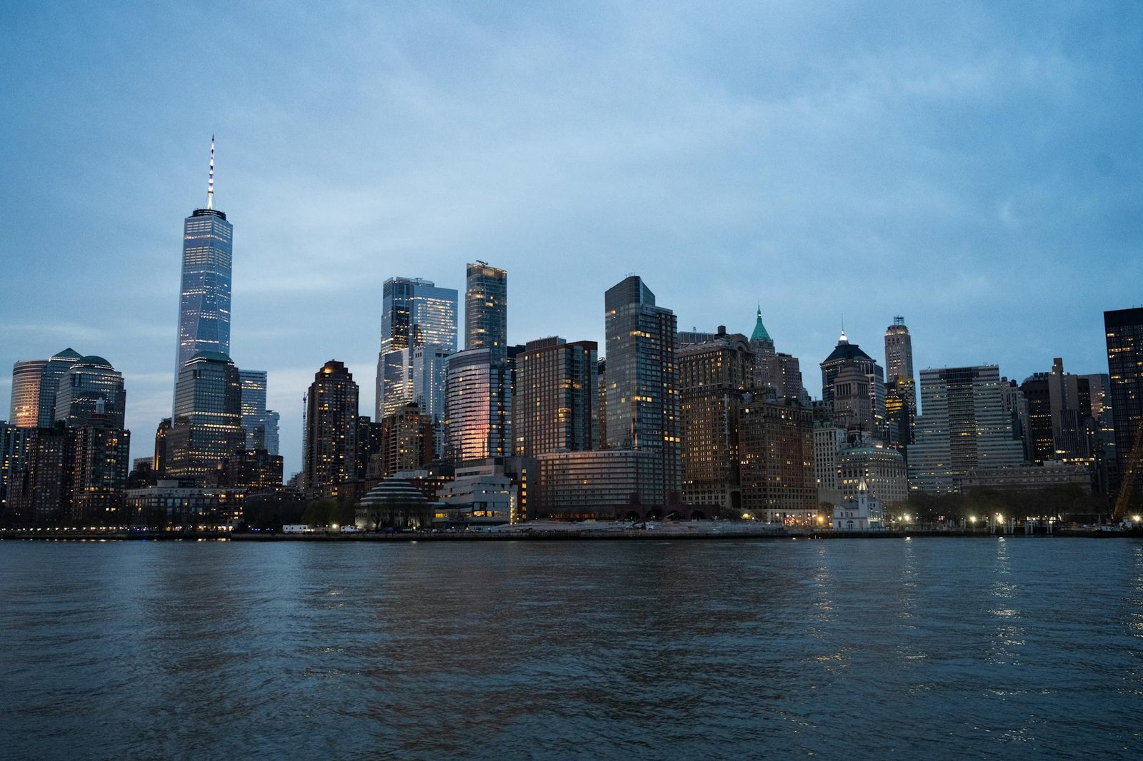 Dramatic view of the New York City skyline at dusk, featuring iconic skyscrapers reflecting on the water.