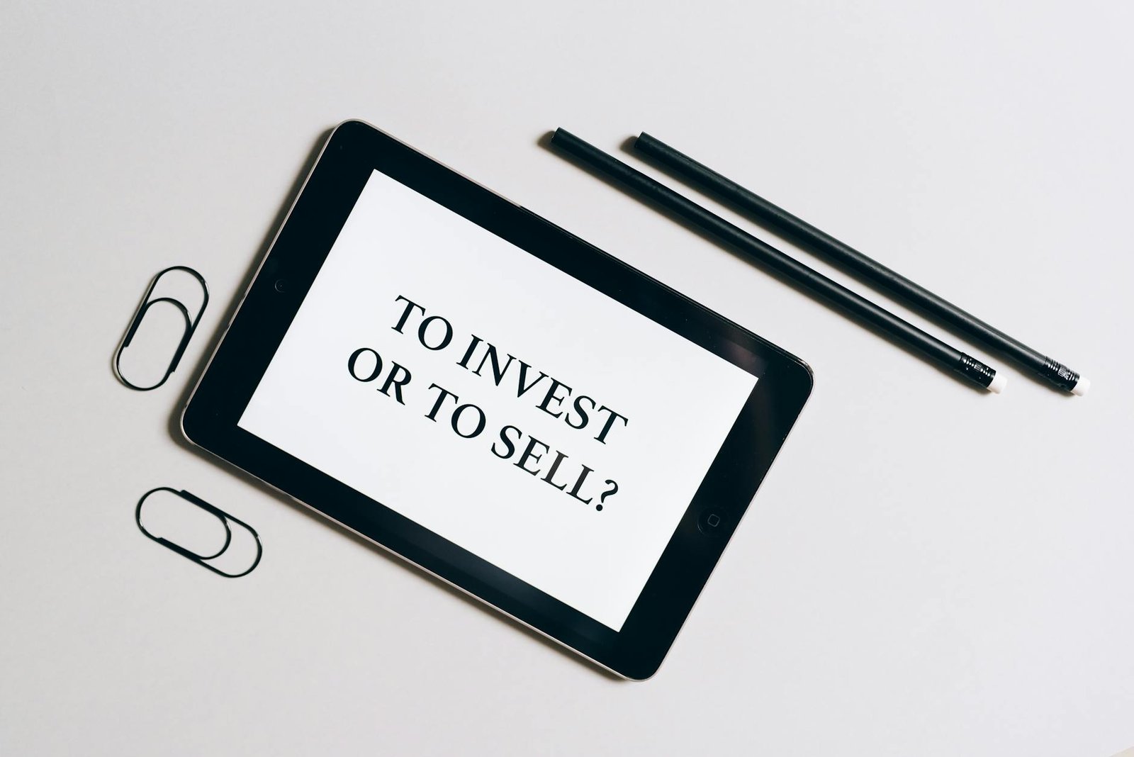 Flat lay of tablet with investment decision text, surrounded by stationery on a white table.