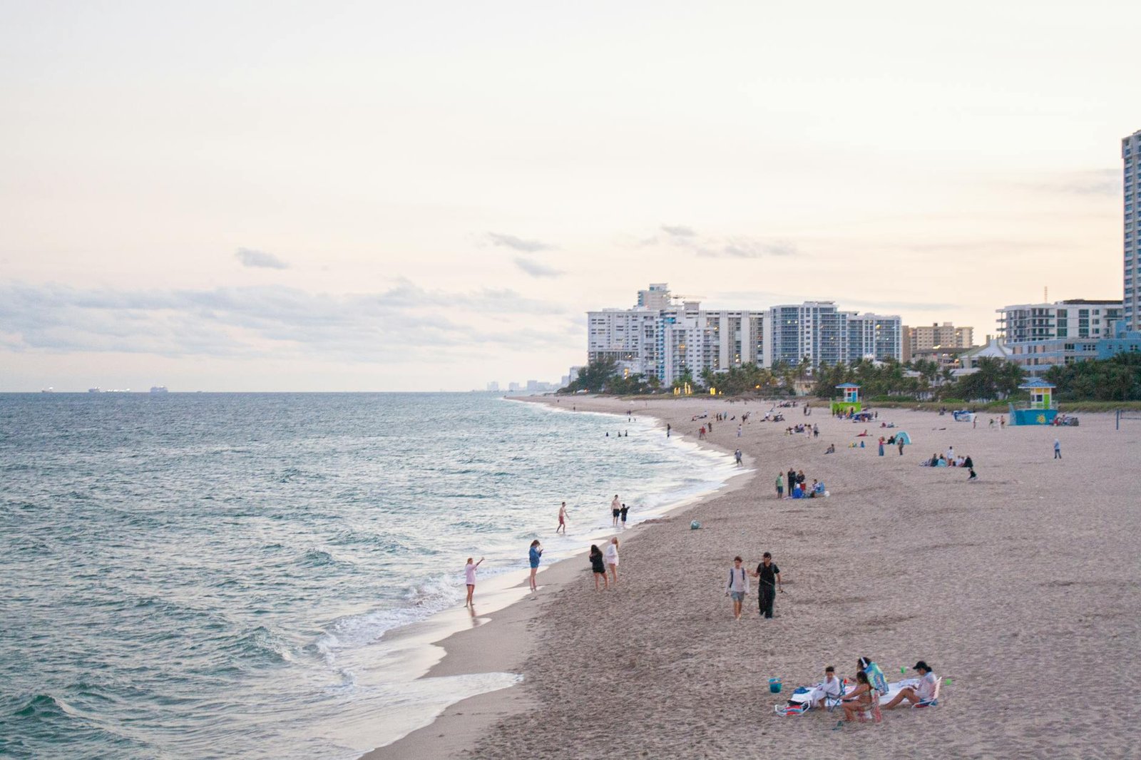 A calming view of a sandy Florida beach at sunset with people enjoying the ocean and distant buildings in sight.