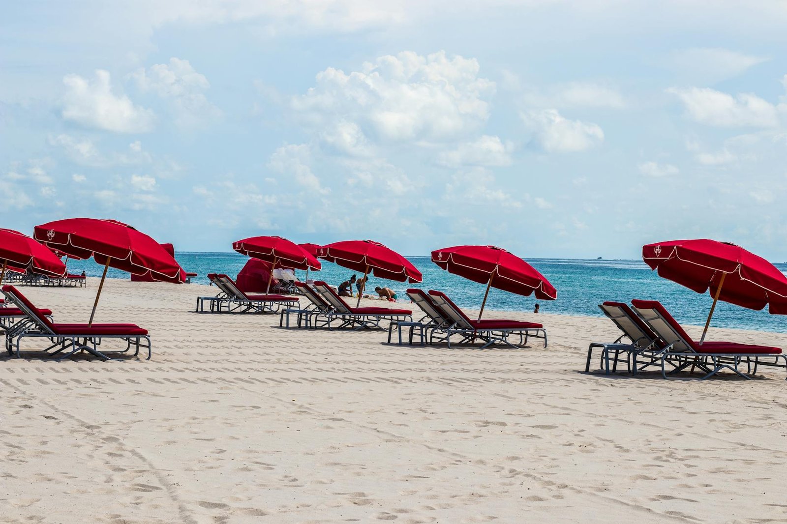 Relaxing Miami Beach scene with red umbrellas and deckchairs on a sandy beach.