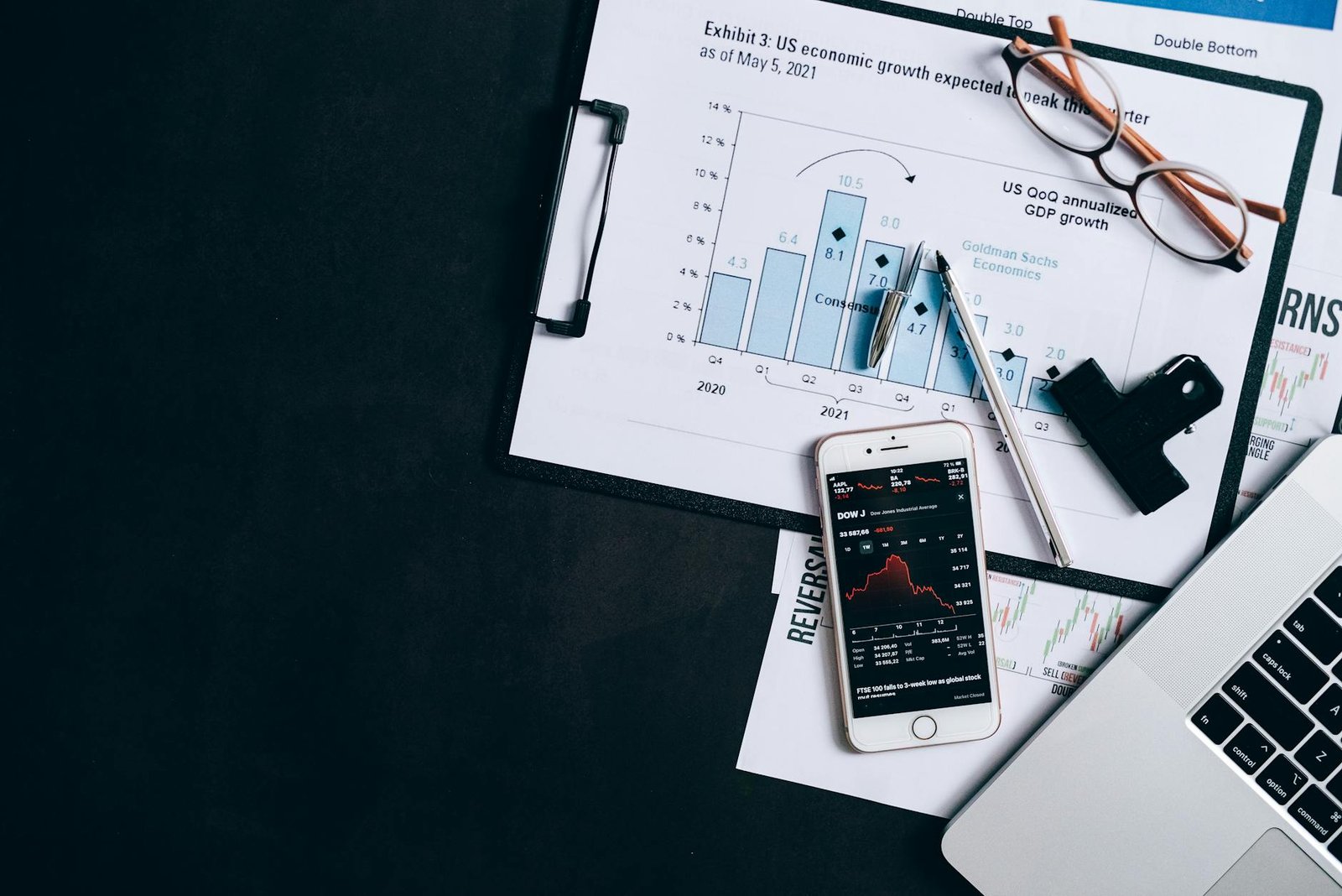 Top view of financial reports, smartphone showing stock market data, and a laptop on desk.